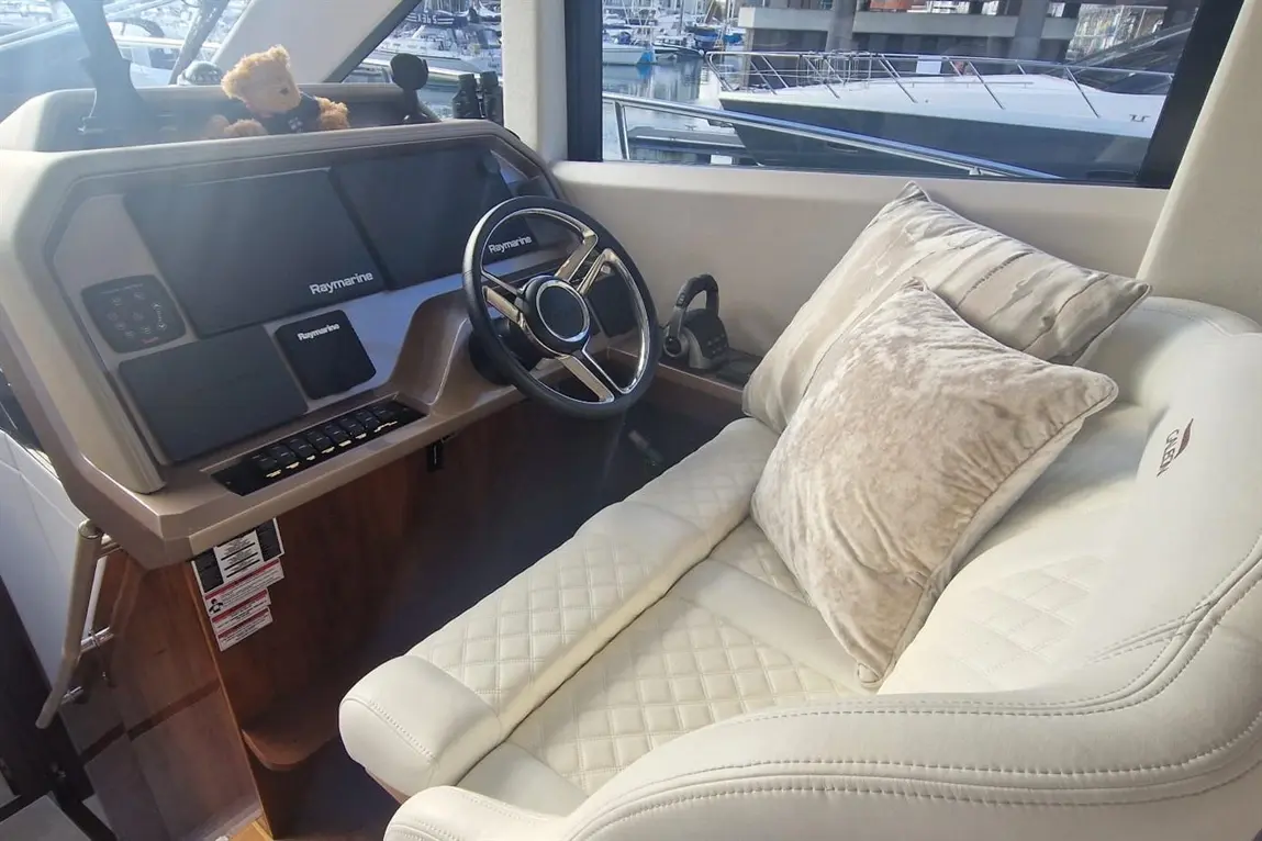 Luxury boat interior featuring a Raymarine dashboard, plush white captain's chair, decorative cushions, and a teddy bear.